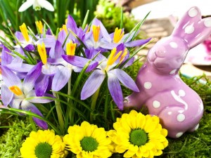 Figurita de un conejo junto a flores lilas y amarillas
