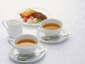 Dos tazas blancas de té con unos petits fours