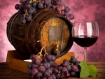 Un barril, una copa de vino y unos racimos de uvas moradas