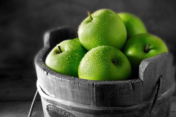 Un cubo de madera con manzanas verdes