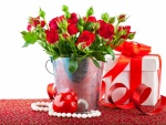 Arreglo floral con rosas rojas junto a una caja de regalo