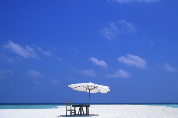 Mesa y silla de madera bajo una sombrilla blanca en la playa