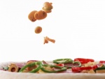 Champiñones y aceitunas cayendo sobre una pizza sin hornear
