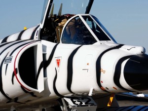 Postal: Un avión de combate pintado de blanco con líneas negras como una cebra