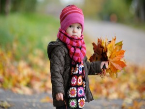 Una niña pequeña recogiendo hojas caídas en otoño