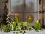 Velas, pinos, bolas y regalos de color verde junto a una ventana en Navidad