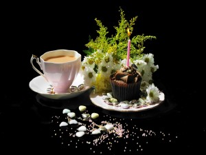 Taza de té junto a una magdalena de cumpleaños y un ramo de margaritas