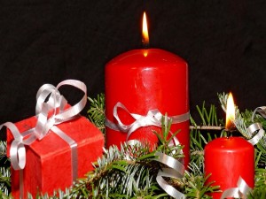 Regalo y velas rojas sobre ramas de pino para decorar en Navidad