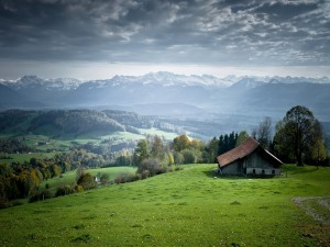 Postal: Cabaña en un verde valle con vistas a las montañas