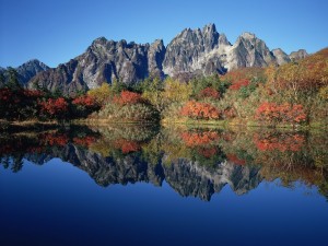 Árboles otoñales y montañas reflejados en el lago