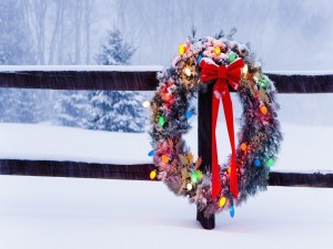 Postal: Corona de Navidad iluminada colgada de una valla bajo la nieve
