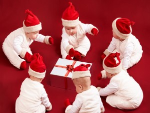 Bebés con gorros de Papá Noel alrededor de un regalo