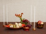 Velas largas y blancas sobre una mesa con frutas y flores