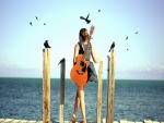 Mujer con su guitarra contemplando el mar