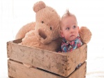 Bebé en una caja junto a un gran oso de peluche