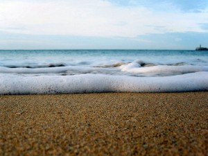 Postal: Espuma de mar sobre la arena de una playa