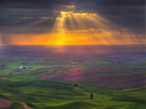 Rayos de sol filtrándose entre las nubes iluminando campos verdes