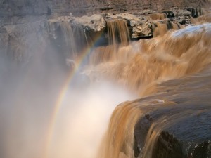 Postal: Arcoíris sobre las cascadas de un río caudaloso