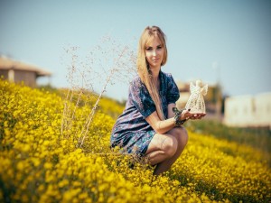 Postal: Chica en un campo de flores sosteniendo la figura de un ángel