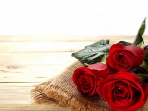 Postal: Tres rosas rojas sobre una mesa