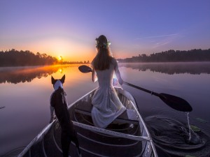 Mujer con un perro remando en un bote al amanecer