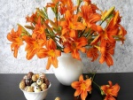 Lirios naranjas en un florero junto a un platillo con bombones