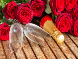 Postal: Ramo de rosas rojas sobre  una botella de champán y dos copas