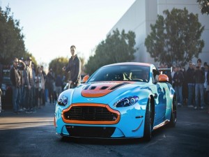 Postal: Gente contemplando un Aston Martin de color azul y naranja