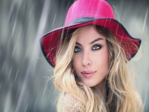 Mujer hermosa con un sombrero de color rosa bajo la lluvia