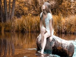 Hermosa mujer sentada en un tronco en el río