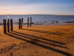 La sombra de unos pilares de madera sobre la playa arenosa