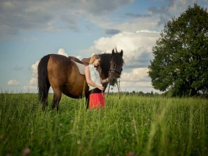Mujer acariciando a un caballo que come hierba fresca