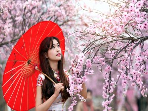 Una mujer con sombrilla roja observando las flores