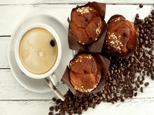 Taza de cappuccino junto a unos muffins de chocolate y granos de café
