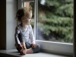 Una niña contemplando la lluvia por la ventana