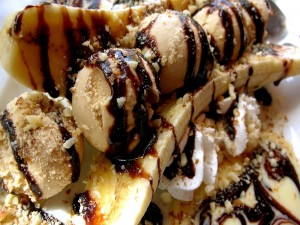 Delicioso postre con plátanos y bolas de helado bañado con chocolate