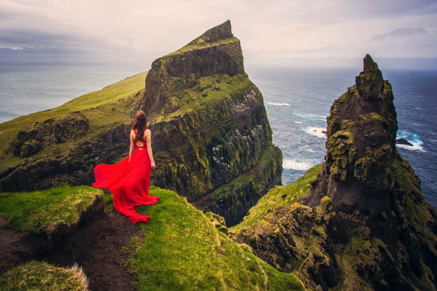 Mujer con vestido rojo sobre un acantilado observando el mar